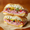 A New Orleans muffuletta cross-section: layered mortadella and salami with chopped olive salad on a round sesame loaf, cut in half on paper.