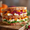 A tall Thanksgiving sandwich on grainy bread, layered with sliced turkey, cranberry sauce, roasted sweet potato and greens, on a wooden board.