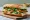 A banh mi on a wooden board, split to show a browned slab of fried tofu, shredded pickled daikon and carrot, cucumber batons, coriander and sliced green chilli against the airy white crumb.