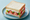 A fruit sando on a pale blue rimmed plate, two slices of soft white bread pressed around whipped cream with halved strawberries and kiwi wedges, the cut side facing the camera.