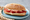 A split baguette on a blue plate, layered with slices of cured Bayonne ham and pale sheep's-milk cheese, a striped cloth beside the plate.