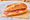 A demi-baguette on brown paper on a marble table, split and filled with slices of dry saucisson over a thick layer of butter.