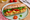 A baguette sandwich on a green plate, filled with curried chicken salad, tomato slices and lettuce, a halved cherry tomato on the plate beside it.