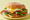 A torta on a round telera roll on a pale yellow plate, stacked with sliced steak, ham, orange cheese, a fried egg, avocado, tomato, lettuce and jalapeño rings.