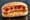 A grilled bratwurst overhanging both ends of a crusty German brotchen, served with mustard.