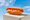 A hot dog in a soft white bun with a zigzag of ketchup and mustard, on a concrete block against a blue sky