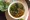 Bowl of red-broth noodle soup with broccoli on a bamboo board, a side plate of lettuce, herbs and lemon