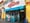 E-Z Stop Deli storefront with a red neon script sign over a blue scalloped awning and an open door