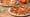 Two Neapolitan pizzas on white plates on a wooden table, one margherita and one pepperoni and sausage, with basil