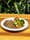 A grilled steak with broccoli, carrots, zucchini and a dinner roll on a white plate on a wooden table