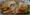 A deli sandwich on a crusty roll, halved on brown paper, with turkey, cheese, lettuce, tomato, olives and pepperoncini