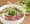 White bowl of combination pho with rare beef, meatballs and tripe, chopsticks across the rim, sprouts and jalapeno beside