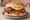 All-Day Breakfast Sandwich: an illustration of bacon, sausage, egg and beans on white bread.