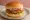 Aloo Tikki Burger: an illustration of potato, chutney, onion and lettuce on burger bun.