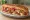 Ayvalık Tostu: an illustration of sucuk, sausage, tomato, pickle and more on bread.