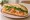 Bánh Mì Cá Hồi Hun Khói: an illustration of salmon, mayonnaise, đồ chua, cucumber and more on bánh mì baguette.