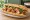Bánh Mì Gà Karaage: an illustration of chicken, đồ chua, cucumber, cilantro and more on bánh mì baguette.