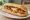 Bánh Mì Ốp La Xúc Xích: an illustration of egg, pork, sausage, đồ chua and more on bánh mì baguette.