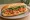 Bánh Mì Tôm Nướng: an illustration of shrimp, đồ chua, cucumber and cilantro on bánh mì baguette.