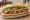 Bánh Mì Vịt Nướng: an illustration of duck, đồ chua, cucumber and cilantro on bánh mì baguette.