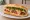 Bánh Mì Xúc Xích Phô Mai: an illustration of sausage, cheese, đồ chua, cucumber and more on bánh mì baguette.