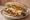 Bondiola Completa: an illustration of lettuce, tomato, onion, chimichurri and more on baguette.