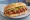 Broodje Babi Pangang: an illustration of pork, onion and cucumber on kaiser roll.