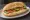 Broodje Hummus: an illustration of hummus, cucumber, tomato and olive oil on kaiser roll.