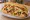 Broodje Kapsalon: an illustration of potato, gouda, lettuce, garlic sauce and more on kaiser roll.