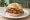 Broodje Pastrami: an illustration of pastrami, mustard and pickle on kaiser roll.