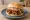 Broodje Pulled Pork: an illustration of pork, bbq sauce and coleslaw on kaiser roll.