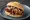 Broodje Saté Babi: an illustration of pork and onion on kaiser roll.