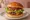 Burger z Wołowiną Angus: an illustration of beef, cheddar cheese, lettuce, tomato and more on burger bun.