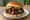 Burnt Ends Sandwich: an illustration of beef, bbq sauce and pickle on burger bun.