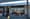Storefront with an Orange Bowl sign, neon Open, Sandwich, Coffee and Teriyaki signs, and patio tables with orange cushions.