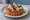 Cretan Dakos Sandwich (Ντάκος): an illustration of tomato, olives, caper, oregano and more.