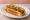 Fenway Frank: an illustration of beef, mustard and pickle on hot dog bun.