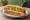 Fenway Frank (Expanded): an illustration of beef, mustard and pickle on hot dog bun.