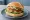 Fischfrikadelle Brötchen: an illustration of fish, onion, parsley and remoulade on bread.