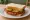 Fried Bologna Sandwich: an illustration of bologna, mustard and pickle on white bread.