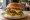 Gurme Burger: an illustration of beef, cheese, lettuce, tomato and more on burger bun.