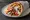Gyros Vegan (Γύρος Vegan): an illustration of mock meat, tzatziki, tomato, onion and more on pita.