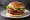 Hamburger Klasyczny: an illustration of beef, lettuce, tomato, onion and more on burger bun.