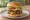 Hamburger Podwójny: an illustration of beef, lettuce, tomato and onion on burger bun.