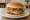 Hamburguesa con Jamón y Queso: an illustration of beef, ham, cheese, lettuce and more on burger bun.