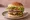 Hamburguesa Doble: an illustration of beef, lettuce, tomato and onion on burger bun.