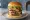 Hamburguesa Triple: an illustration of beef, lettuce, tomato and onion on burger bun.