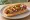 Hot Dog con Frijoles: an illustration of sausage and beans on hot dog bun.