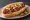 Hot Dog Estilo Sonora: an illustration of sausage, bacon, beans, tomato and more on telera roll.