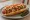 Hot Dog Tijuanense: an illustration of sausage, bacon, tomato, onion and more on hot dog bun.